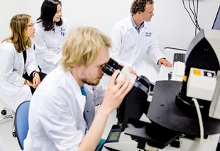 Researchers in white lab coats using a microscope and lab equipment in a laboratory.