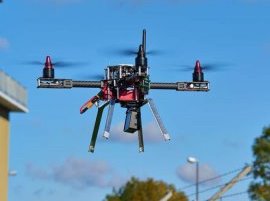 Drone, der flyver i luften udendørs mod blå himmel.