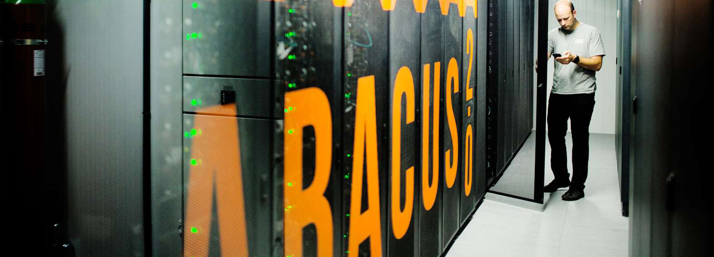 Person i et serverrum ved rackskabe med orange tekst "ABACUS" og grønne indikatorlys.