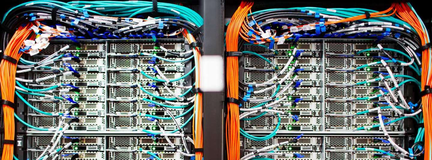 Two packed server racks with numerous connected network cables and bundled orange fiber lines in a data center.