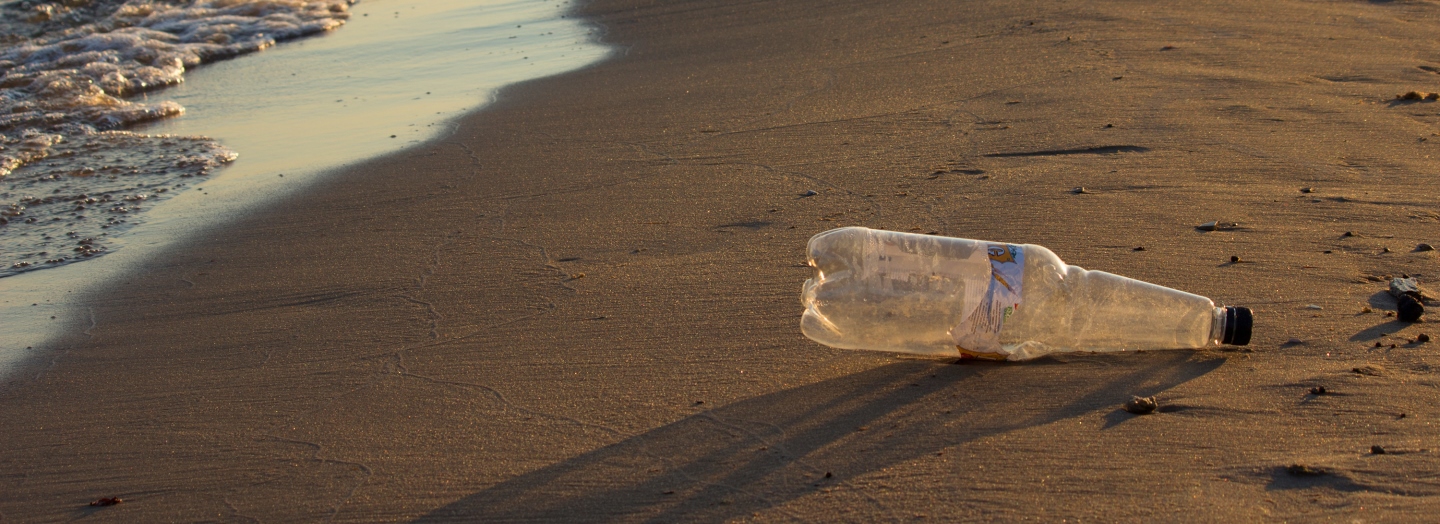Gennemsigtig plastikflaske ligger på sandet ved vandkanten på en strand.