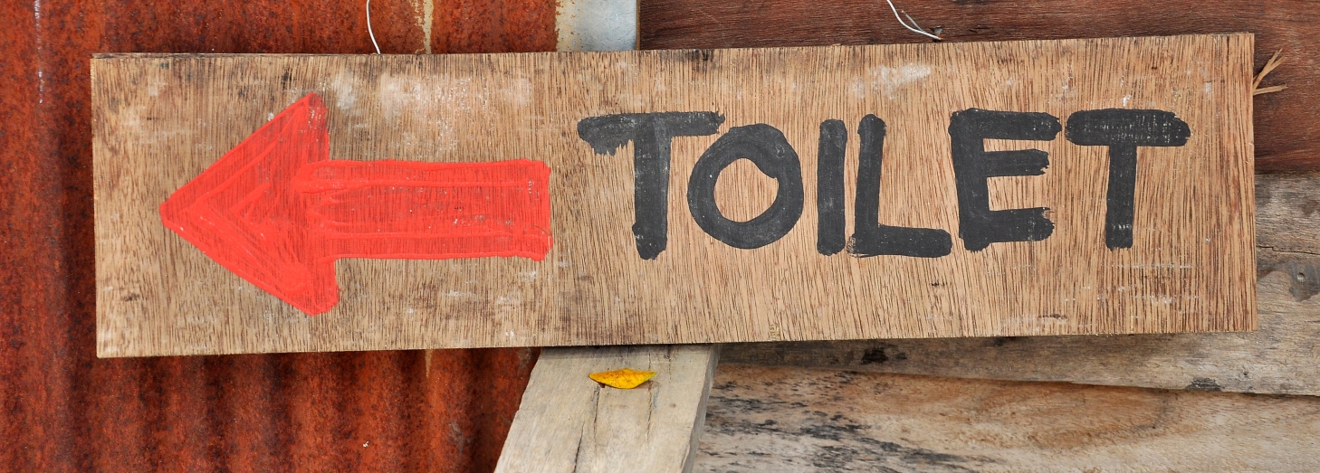 Håndmalet træskilt med rød venstrepil og teksten "TOILET".