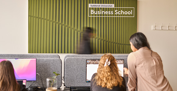 Study area at the University of Southern Denmark Business School with students working in front of a marked green background.