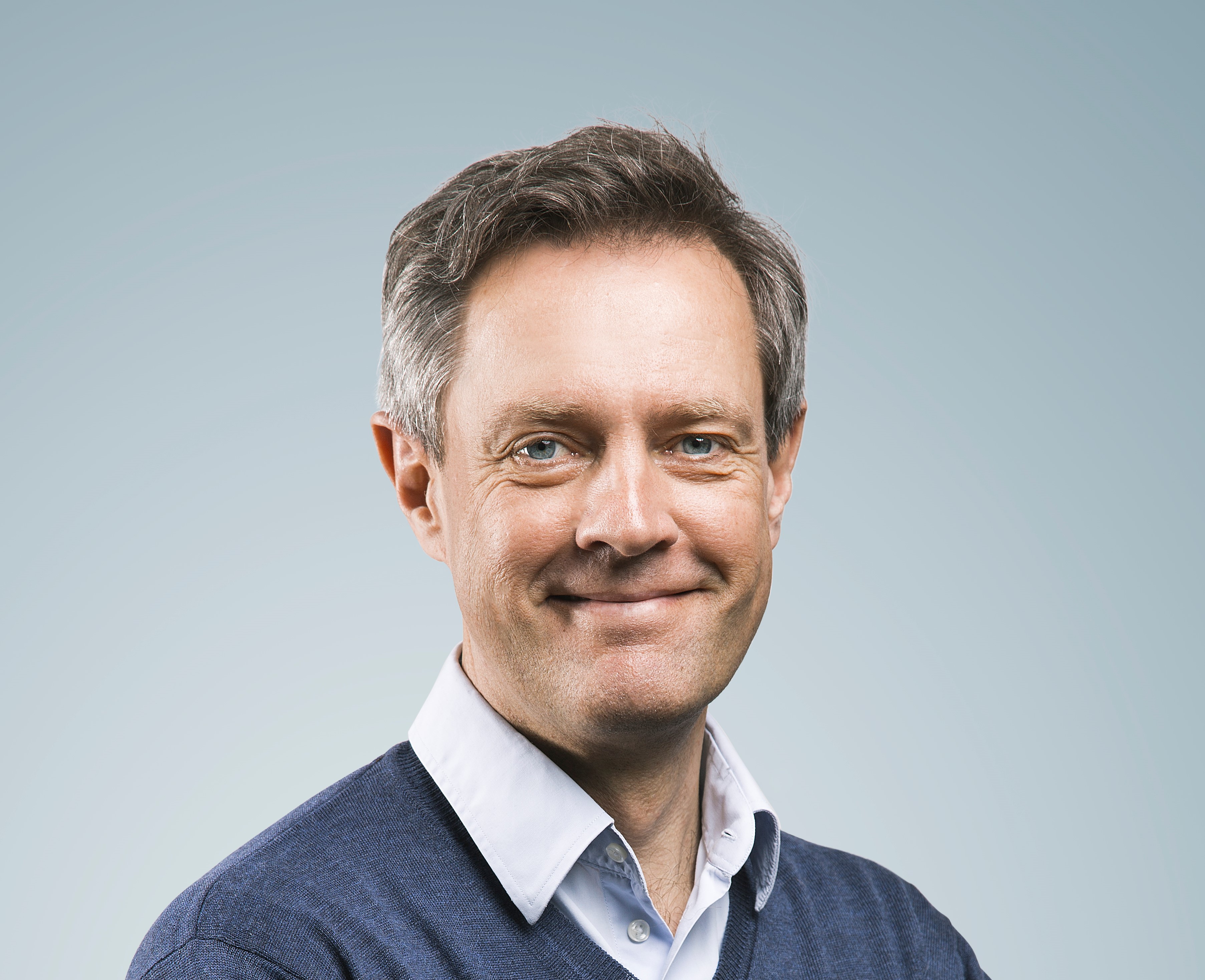 Portræt af Jan Hartvigsen SDU i blå trøje og lys skjorte foran en lyseblå baggrund.