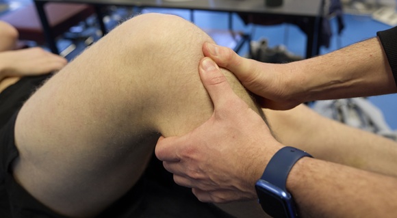 Fysioterapeut behandler knæskade med manuel terapi – nærbillede af hænder, der undersøger patientens knæ under behandling i klinik.