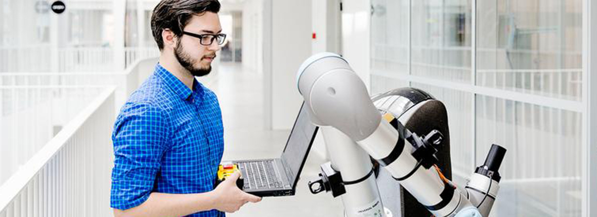 Studerende med bærbar computer ved en industriel robotarm på civilingeniør i robotteknologi bachelor på SDU.