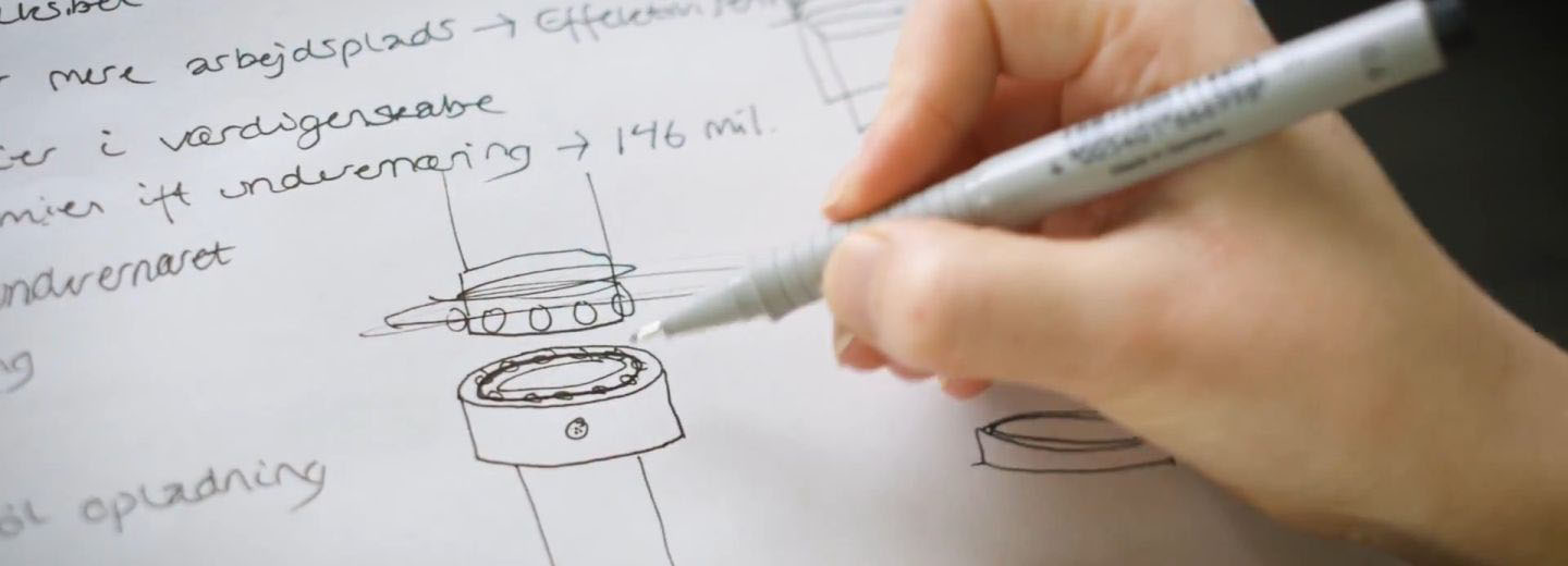 Hand drawing technical concept sketches on paper beside handwritten notes reading "arbejdsplads", "i værdigerseabe", "ift undervemg" and "146 mil."