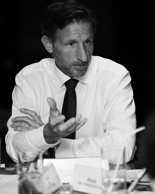 Black-and-white photo of a man in a shirt and tie gesturing during a meeting.