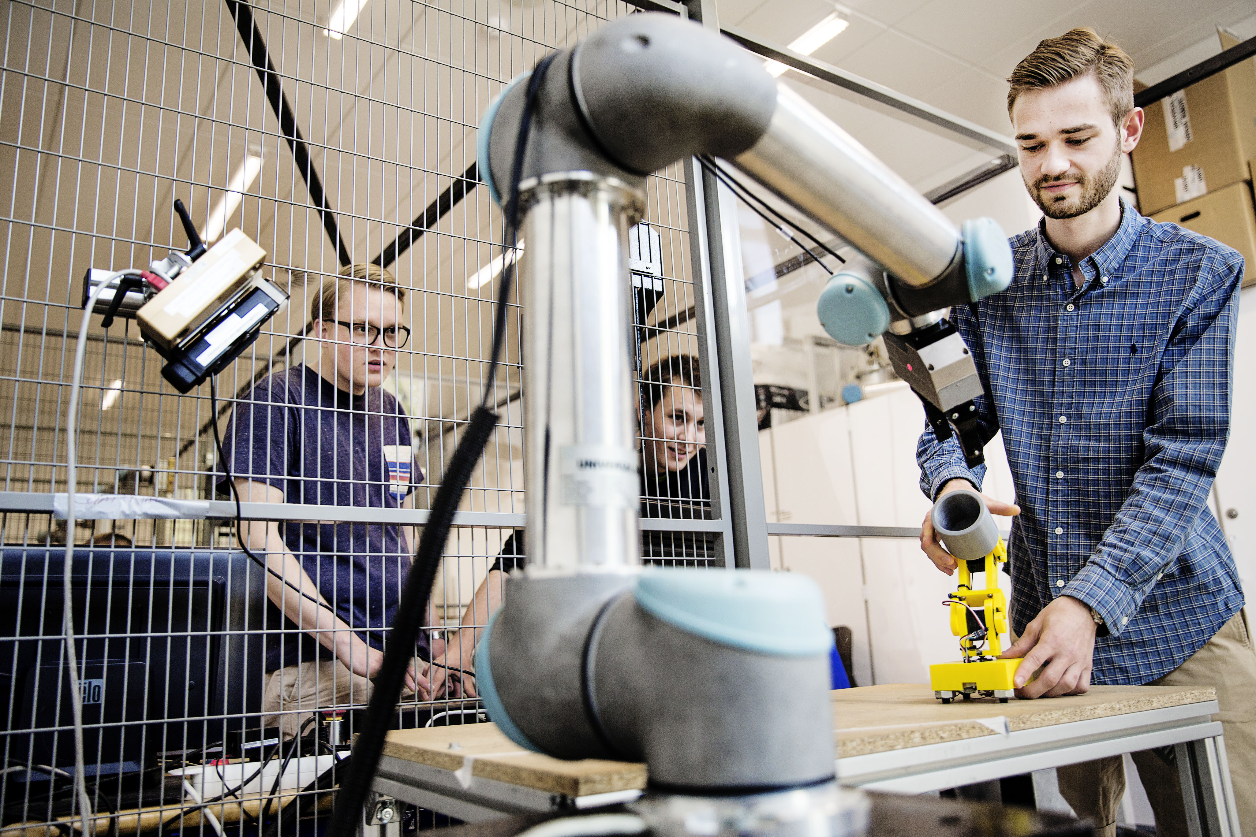 Studerende arbejder med en universal robot i et laboratorie, mens andre ser på bag et sikkerhedsbur.