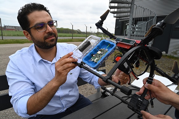 Mand undersøger en åben elektronikenhed ved en stor drone udendørs.