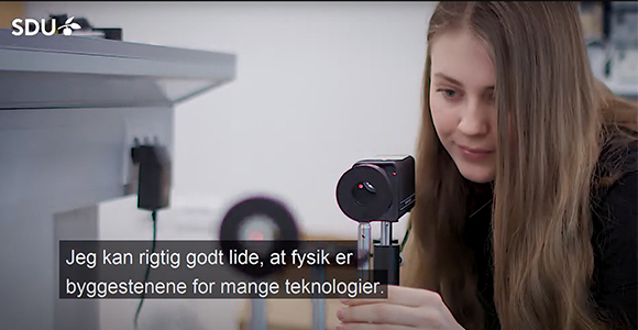 Studerende justerer laboratorieudstyr i et laboratorie med "SDU"-logo og teksten "Jeg kan rigtig godt lide, at fysik er byggestenene for mange teknologier."