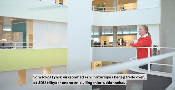 Kvinde i rød jakke står ved et gelænder i et moderne atrium med teksten "Som lokal fynsk virksomhed er vi naturligvis begejstrede over, at SDU tilbyder endnu en civilingeniør-uddannelse." nederst i billedet.