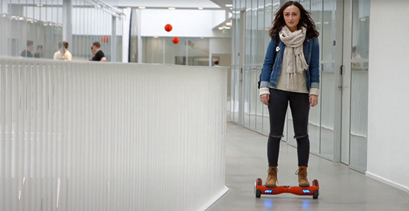 Kvinde, der kører på et orange hoverboard i en moderne kontorgang.