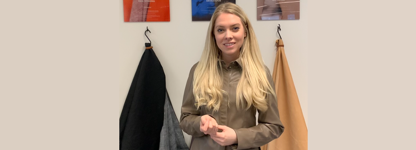 Christina Volf står indendørs foran en lys væg med ophængte materialer og prøver.