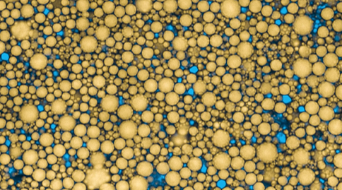 Close-up of numerous golden spherical particles in different sizes on a blue background.