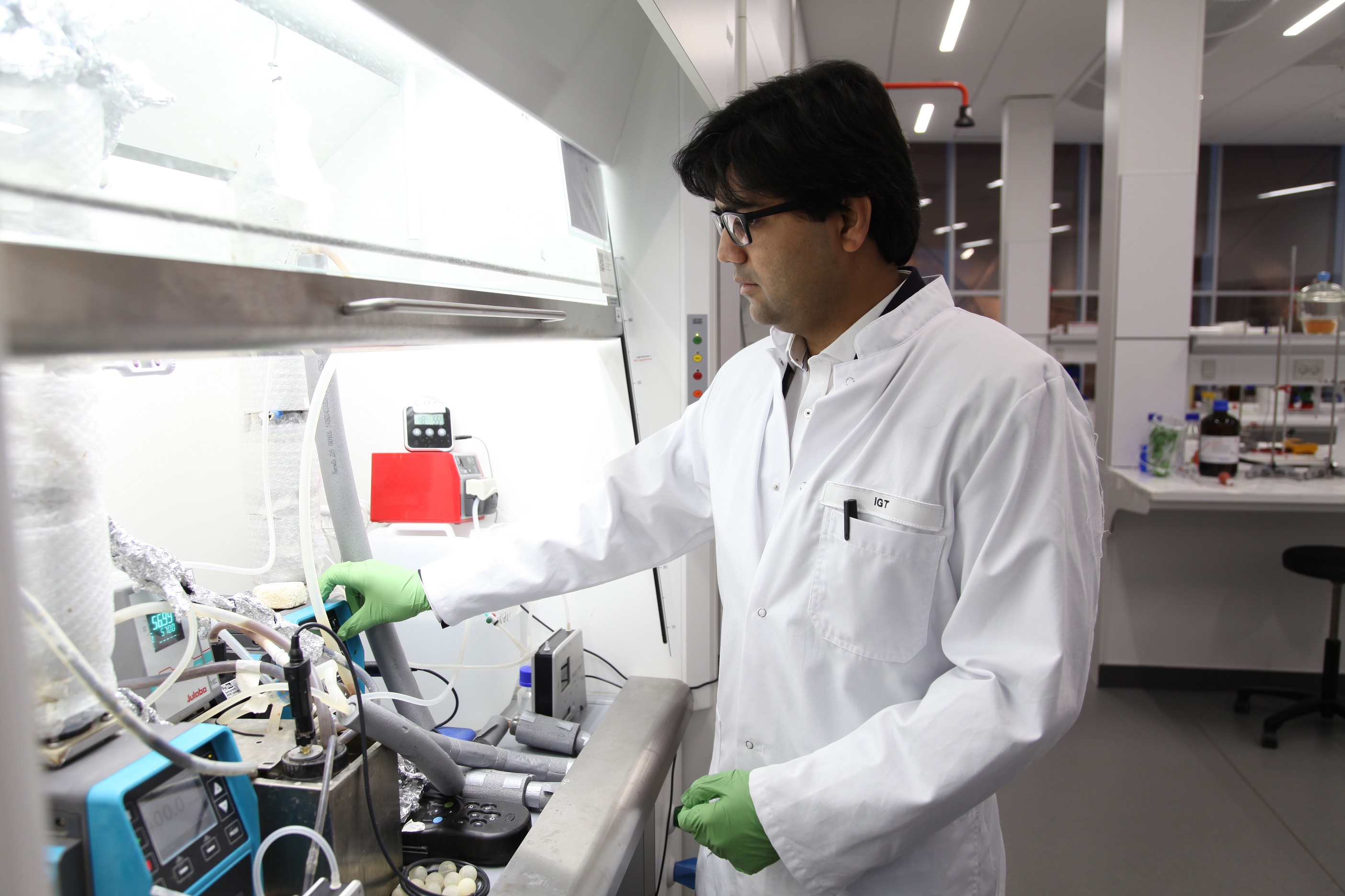 Person i laboratoriekittel arbejder med udstyr og slanger ved en oplyst laboratoriearbejdsstation.