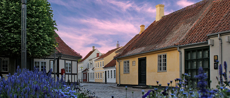 Cobbled street with pastel houses at dusk Cobbled street with pastel houses, red-tiled roofs, purple flowers, and a pink-blue evening sky.