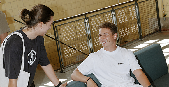 Young woman and young man smiling and talking beside a couch in an indoor common area.
