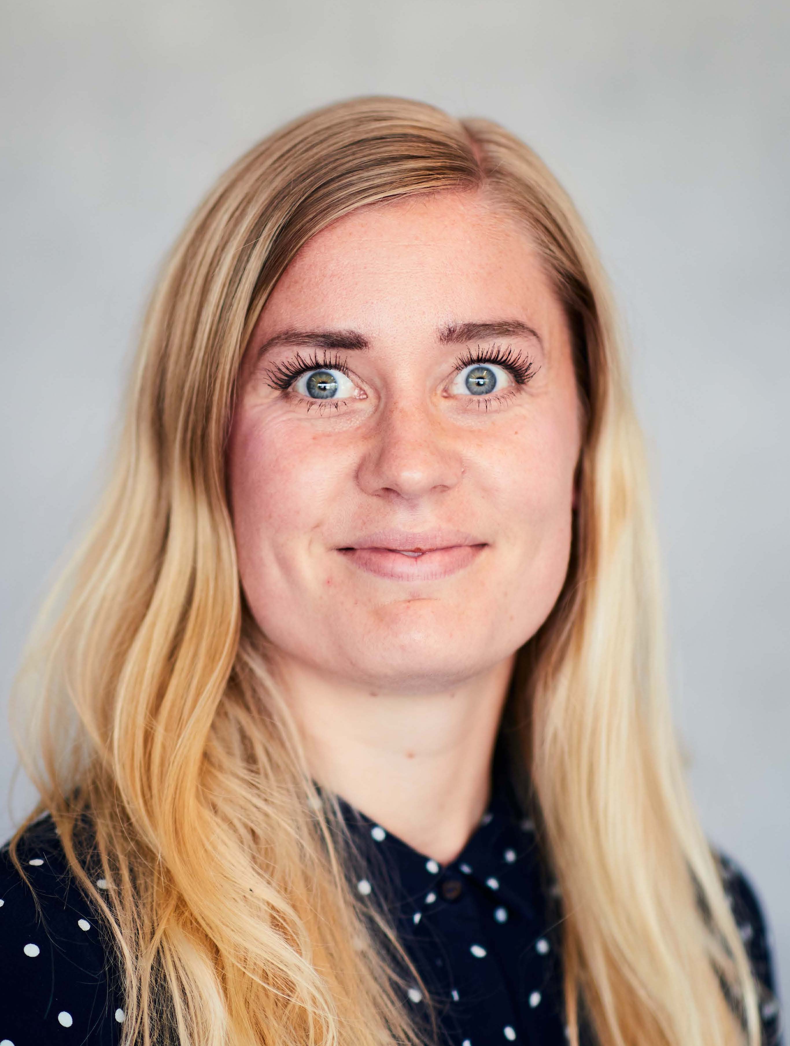 Portræt af Sofie K Nærportræt af Sofie K med langt lyst hår og mørk prikket bluse foran en grå baggrund.