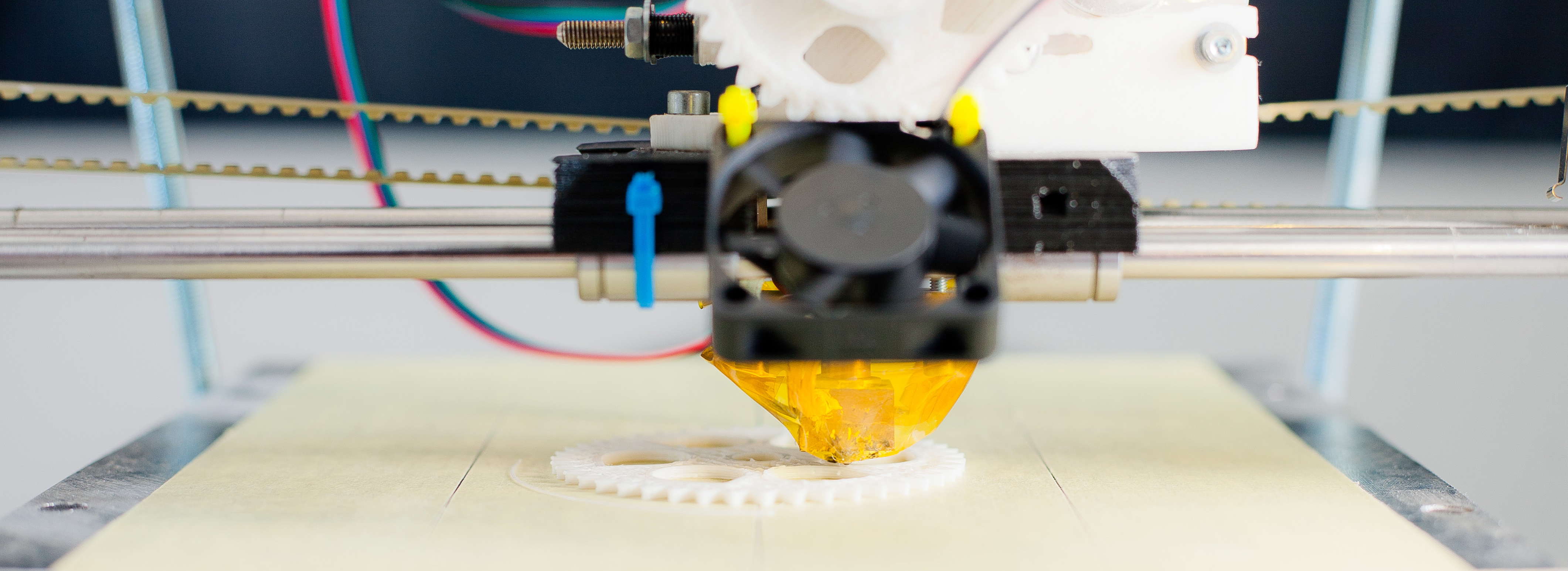 3D-printerhoved, der printer hvide tandhjul på en byggeplade.
