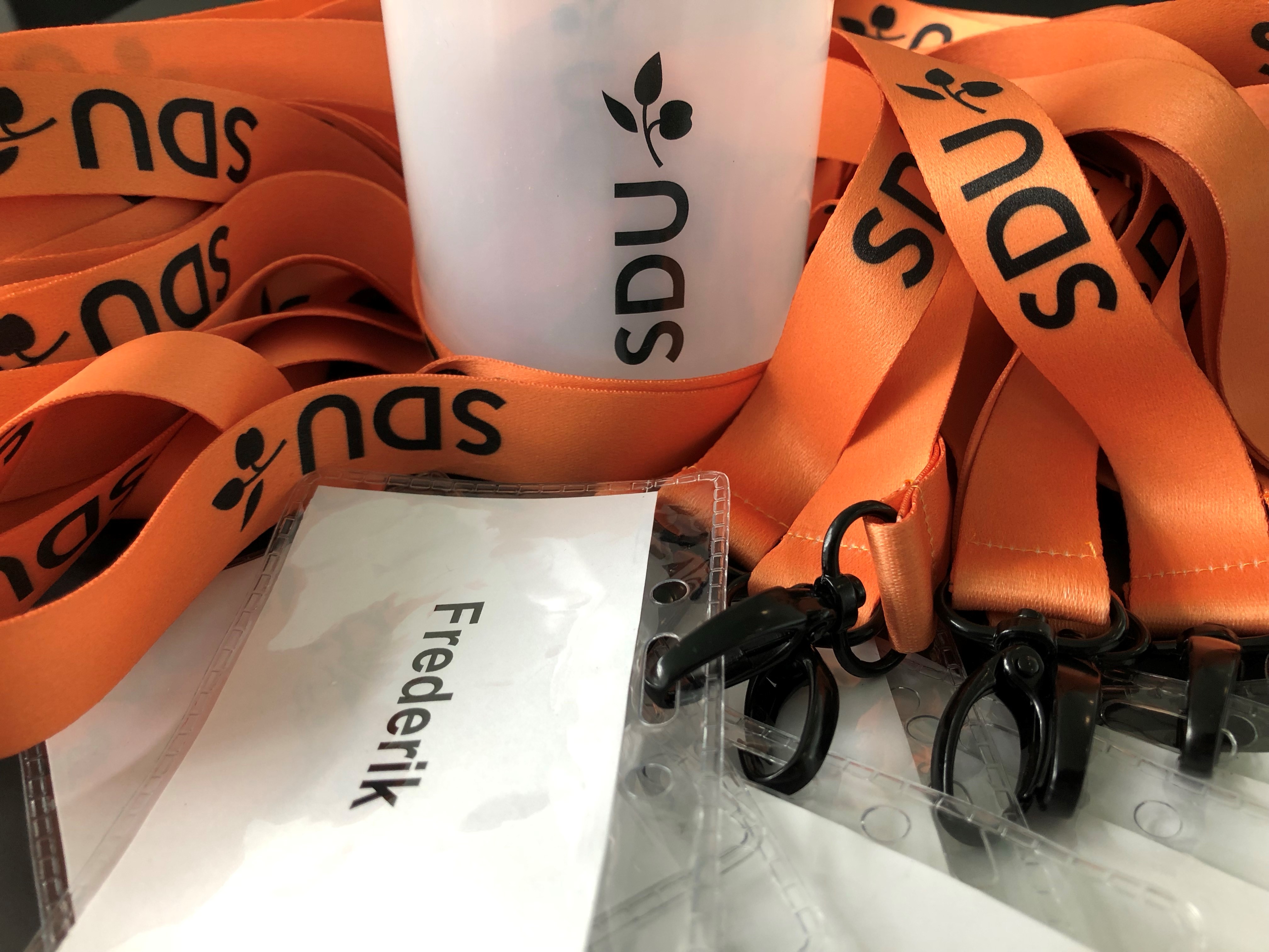 Orange "SDU"-halsbånd omkring en hvid "SDU"-kop og et navneskilt med "Frederik".