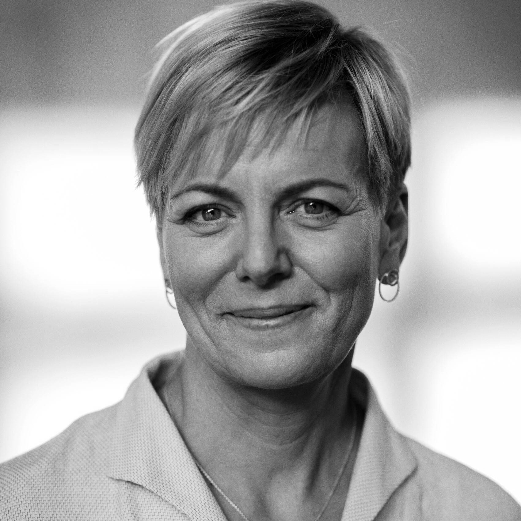 Sort-hvidt nærbillede af en smilende kvinde med kort hår, øreringe og blazer.