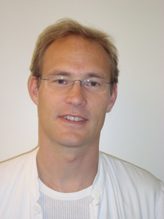 Portræt af lars Dysager med briller og hvid overdel mod en neutral baggrund.