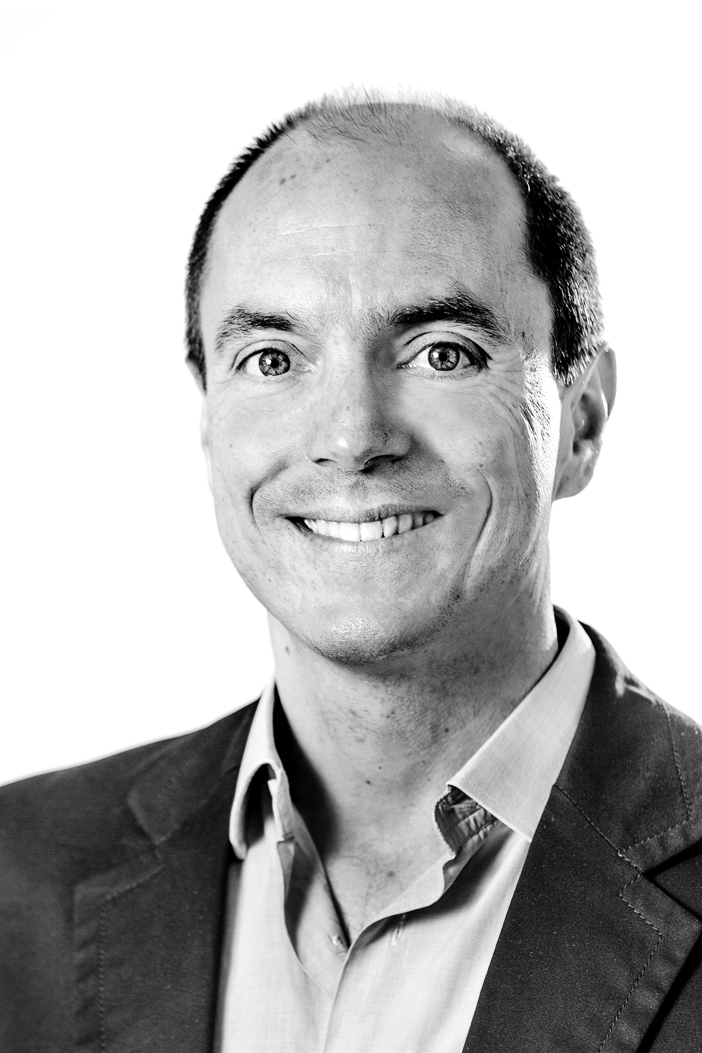 Black-and-white headshot portrait of a smiling man Black-and-white headshot of a smiling man in a blazer and collared shirt.