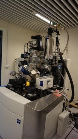 Large laboratory scientific instrument with metal chambers, cables, and attached modules in an indoor research setting.