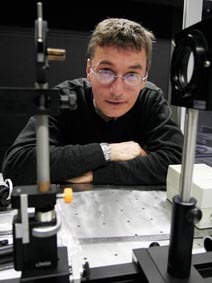 Man with glasses leaning over a laboratory optical table surrounded by scientific equipment.
