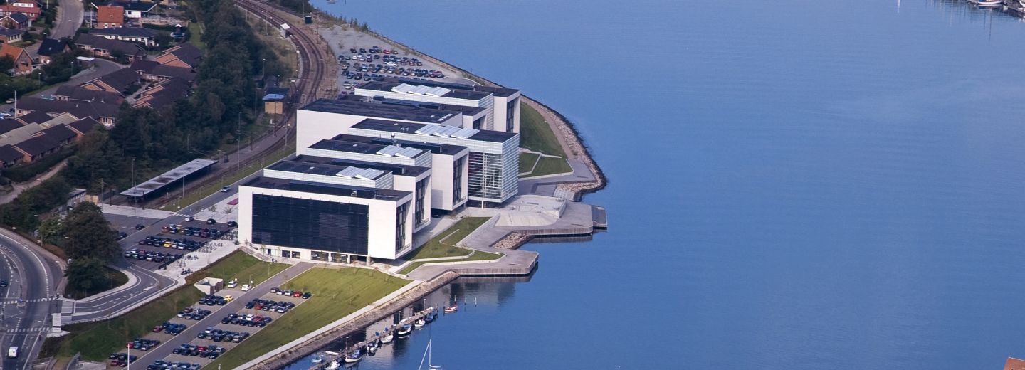 Luftfoto af Alsion i Sønderborg ved vandet med parkeringspladser, vej og jernbane.