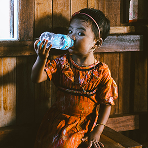 Lille pige i en hytte i Myanmar, der drikker vand af en plastikflaske
