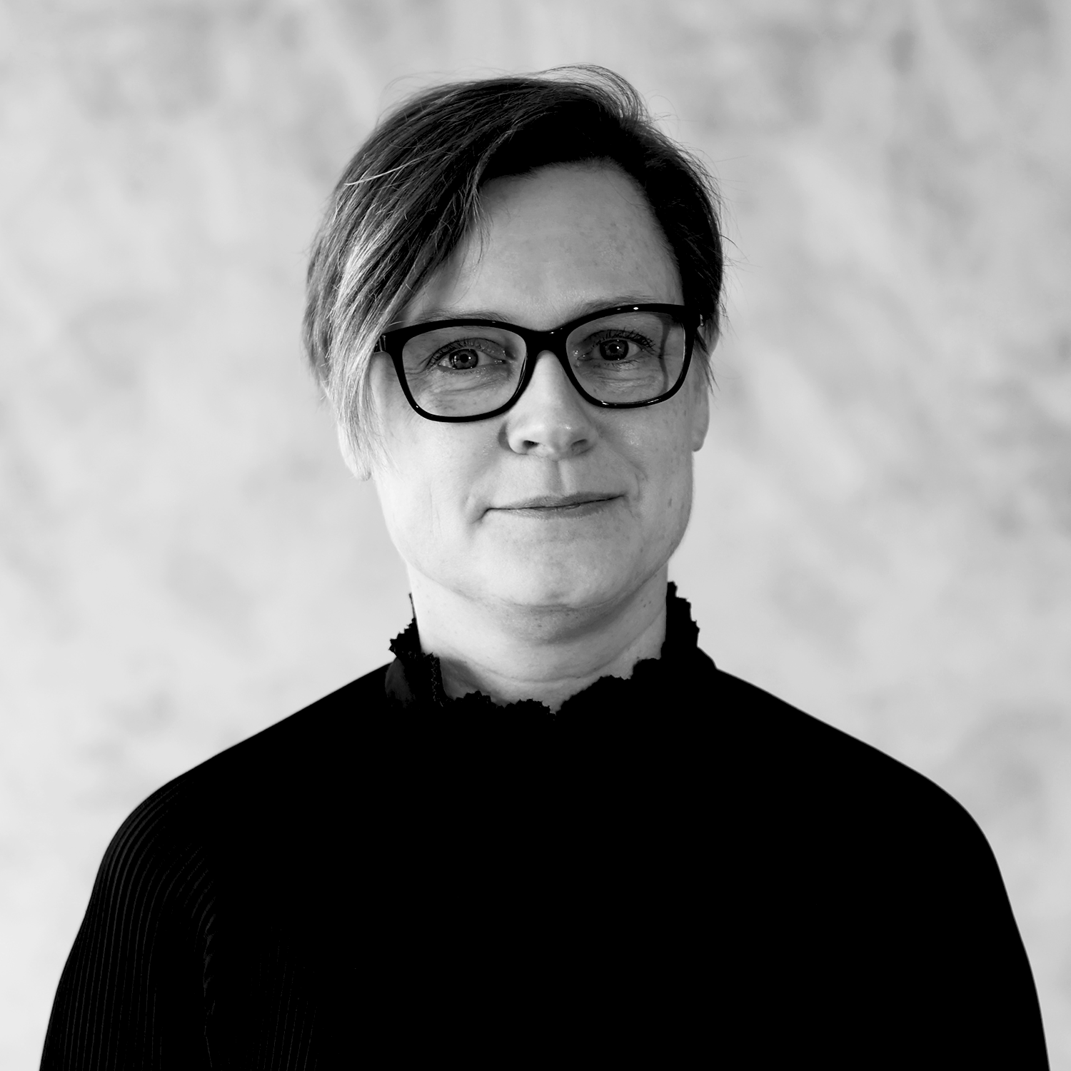 Sort-hvidt portræt af en person med kort hår, mørke briller og mørk højhalset trøje.