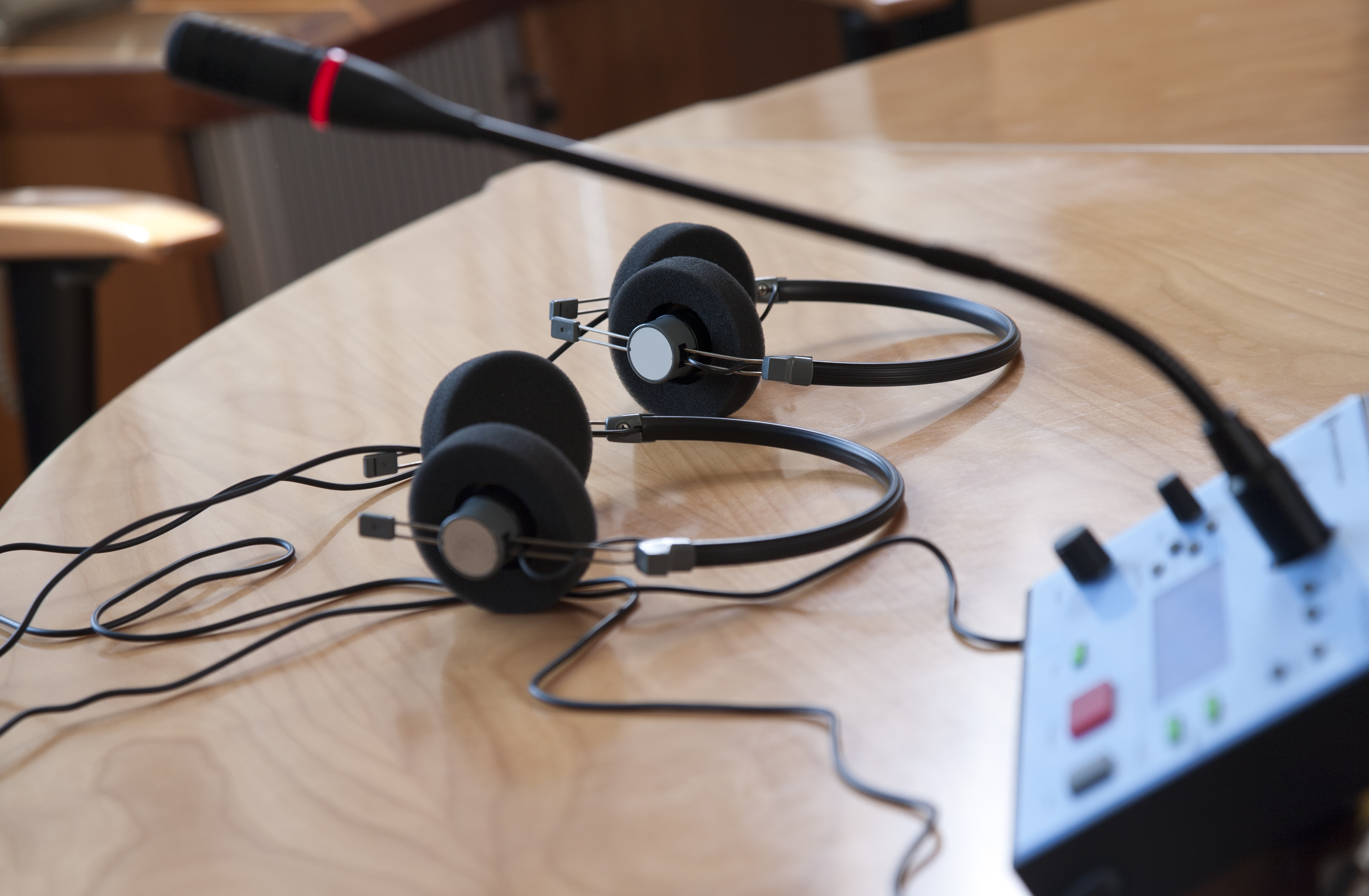 To sorte headsets og en bordmikrofon på et lyst træbord i et møde- eller konferencerum.
