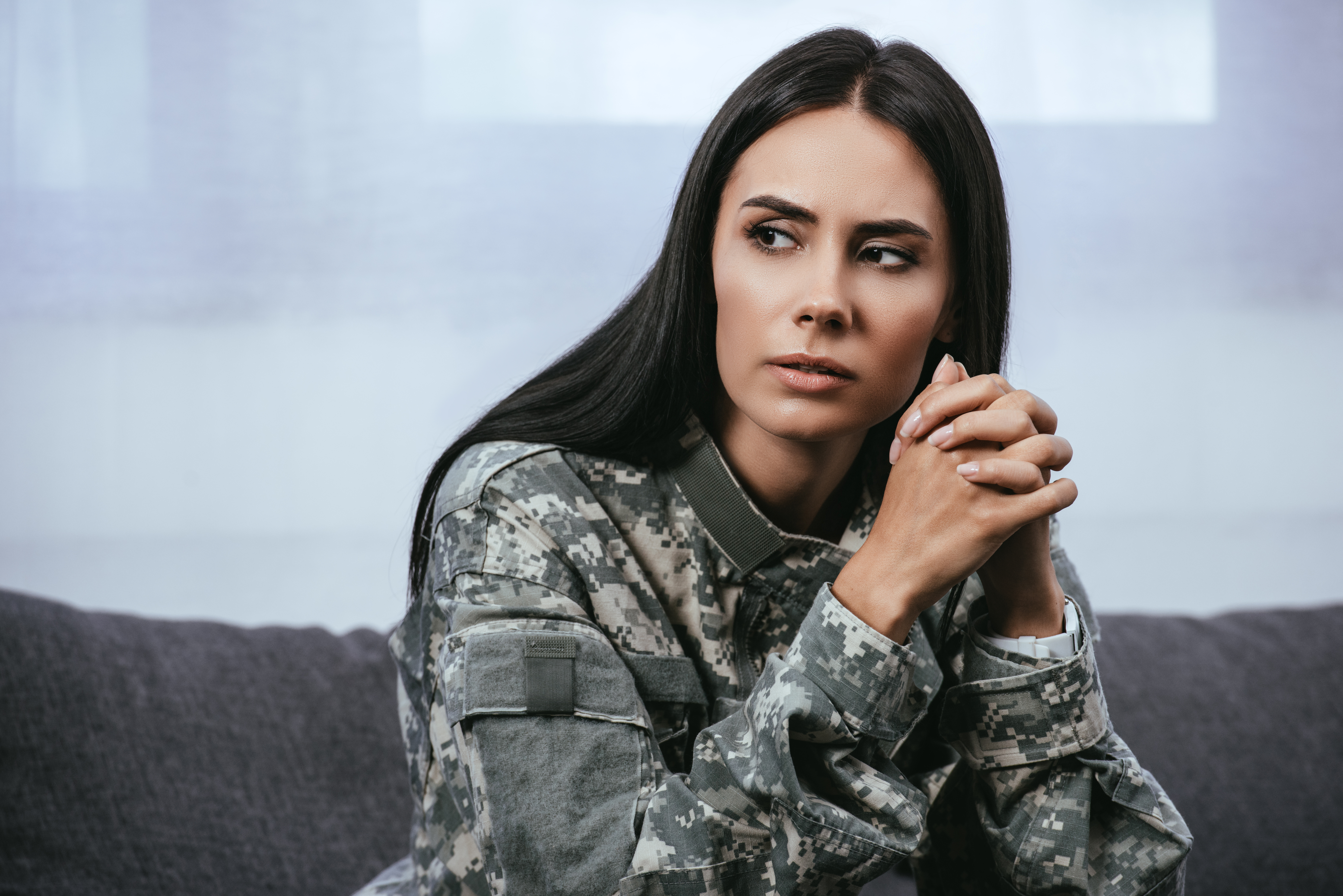 Llose-up portrait of thoughtful female soldier in military uniform with ptsd sitting on couch and looking away
