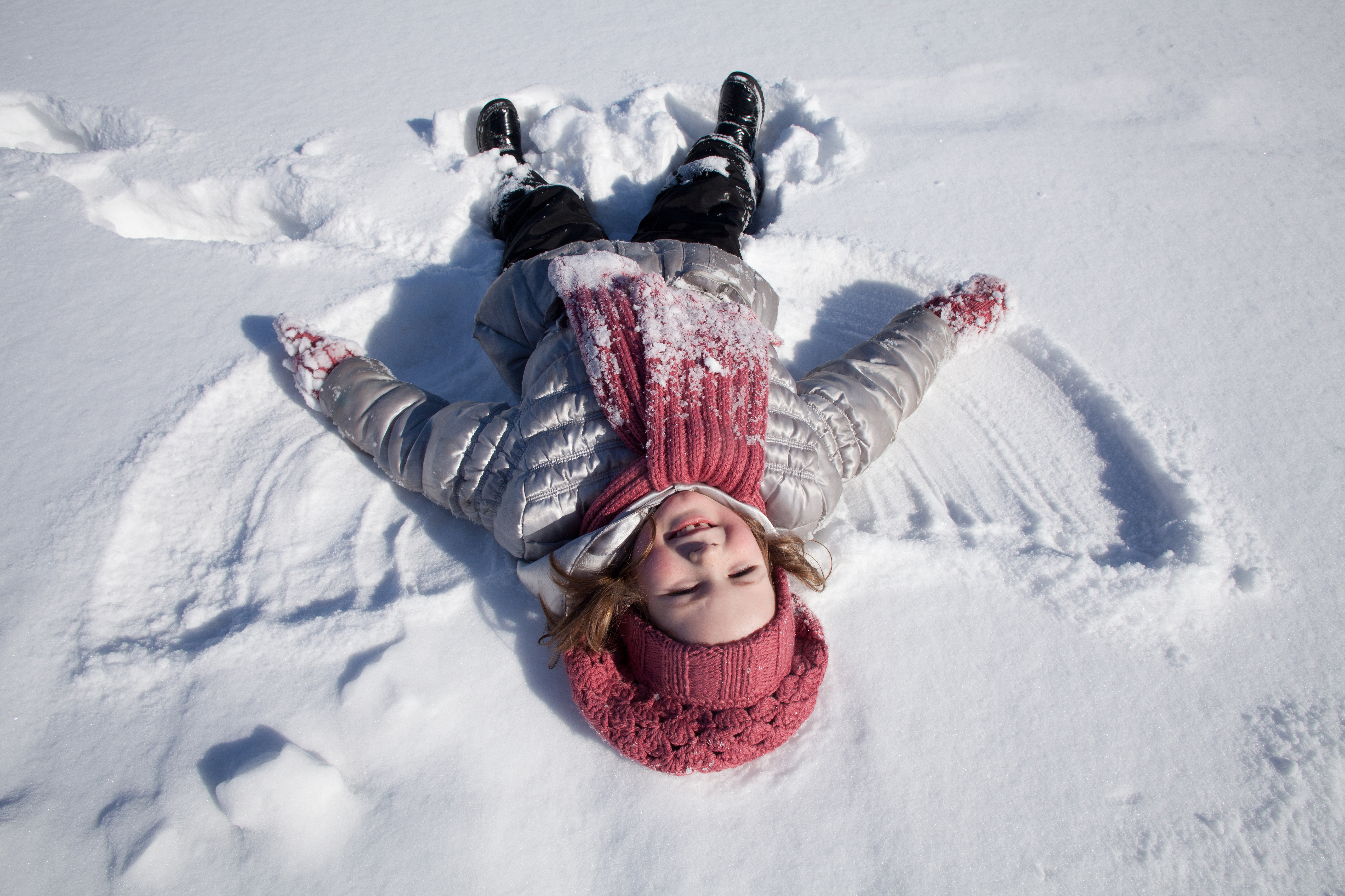 Smiling girl in pink cap and scarf lays on snow