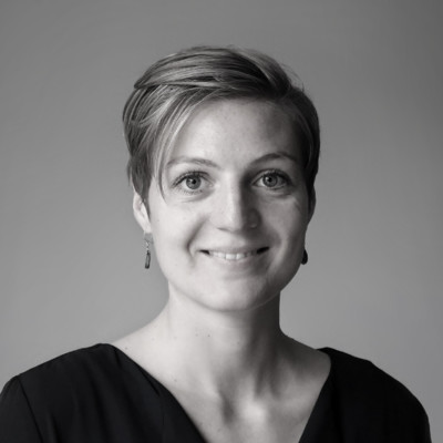 Black-and-white headshot portrait of a smiling woman Black-and-white portrait of a smiling woman with short hair in a dark top against a plain background.