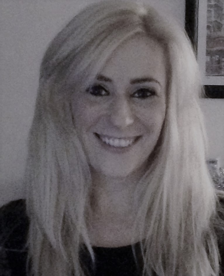 Close-up indoor portrait of a smiling woman with long blonde hair.
