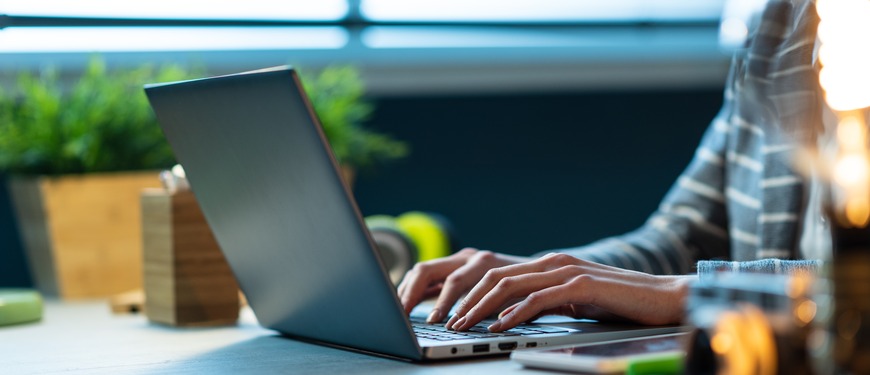 Person skriver på en bærbar computer ved et skrivebord på et kontor.