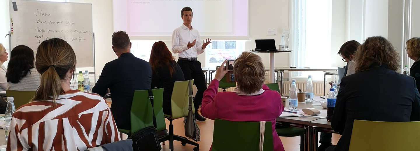 Underviser holder præsentation for en gruppe deltagere i et mødelokale.