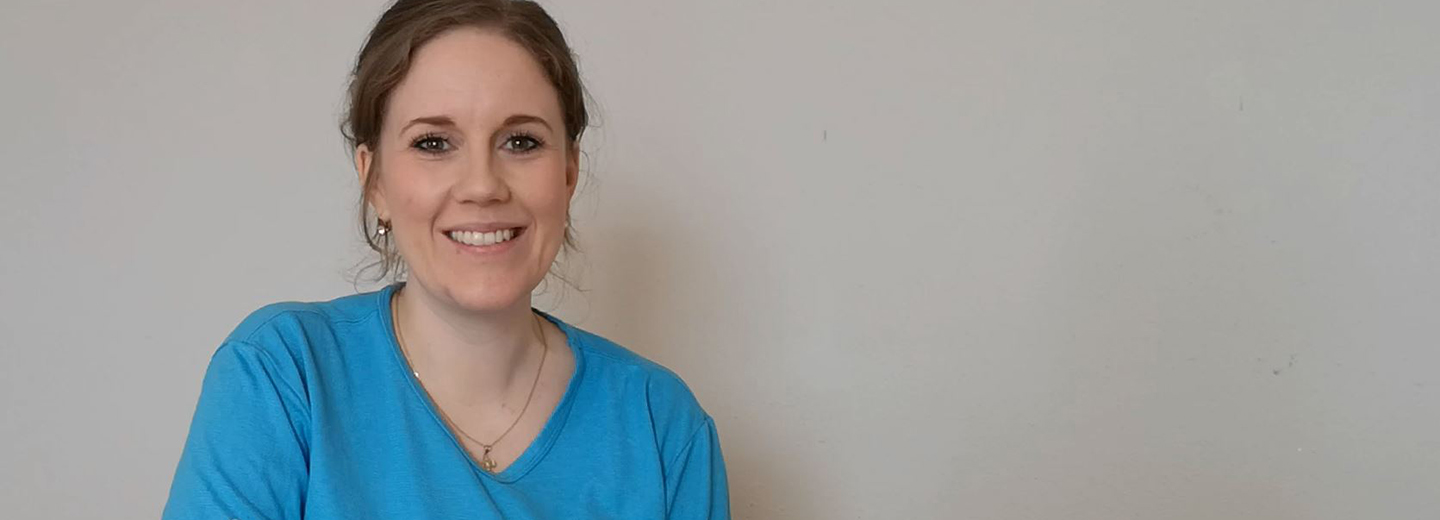 Smilende kvinde i blå trøje foran en lys væg.
