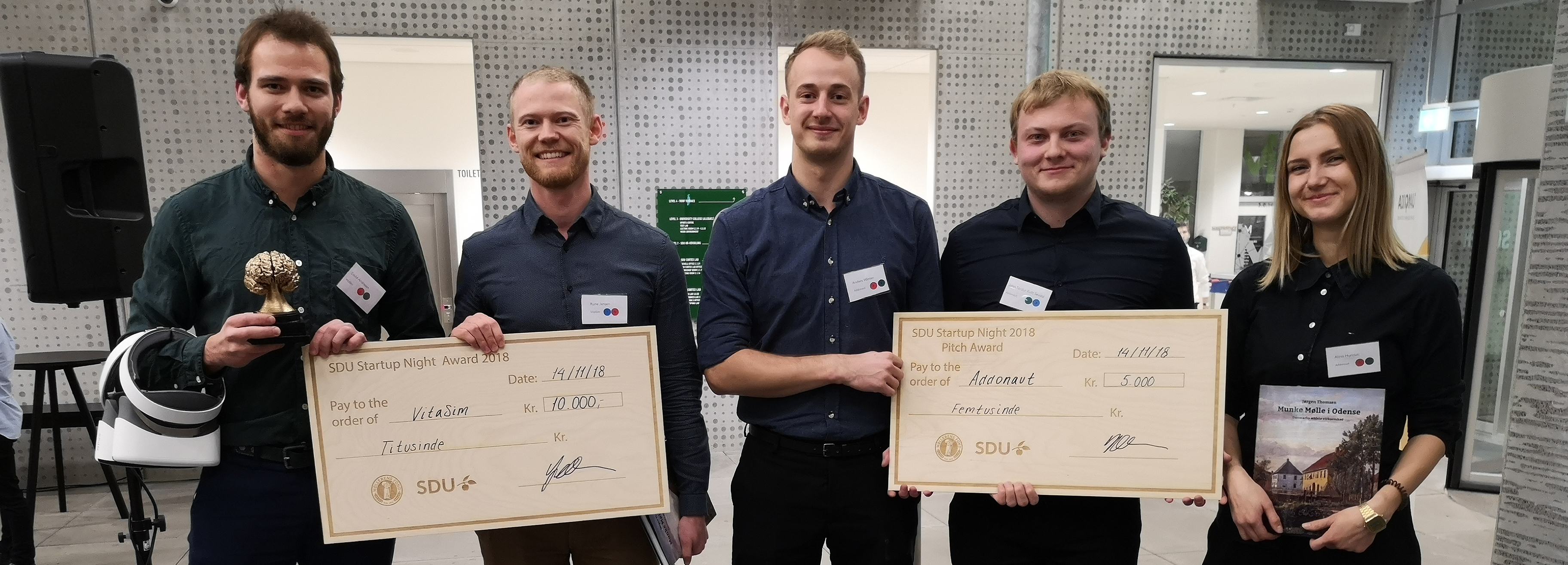 Fem deltagere poserer med priser og checks ved SDU Startup Night 2018, herunder "VitaSim" og "Addonavt".