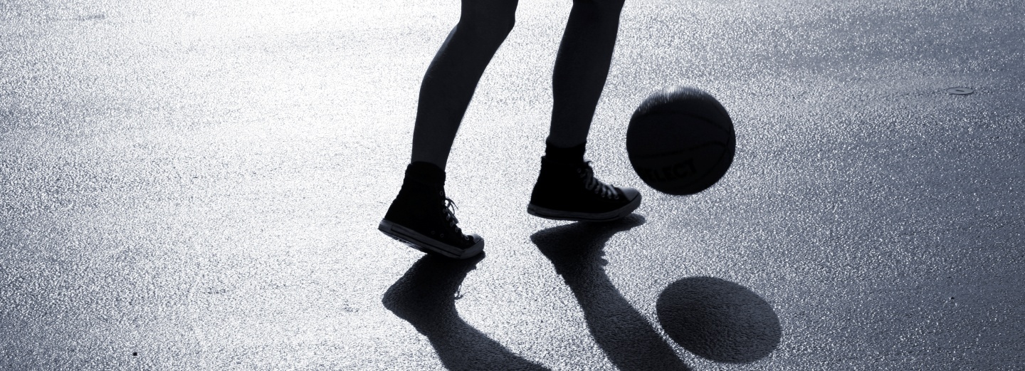 Benene på en person og en basketball over våd asfalt med skygger.