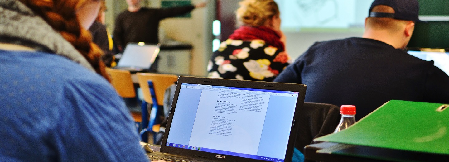 Studerende i et klasseværelse med en bærbar computer i forgrunden og "ASUS" på skærmrammen.