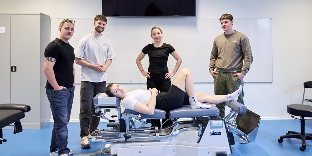 Tre mænd og to kvinder i et lokale, hvor den ene kvinder ligger på en kiropraktorbriks