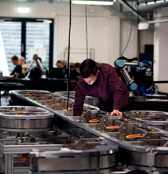 SDU student examining industrial machinery with robotic arms in the background.