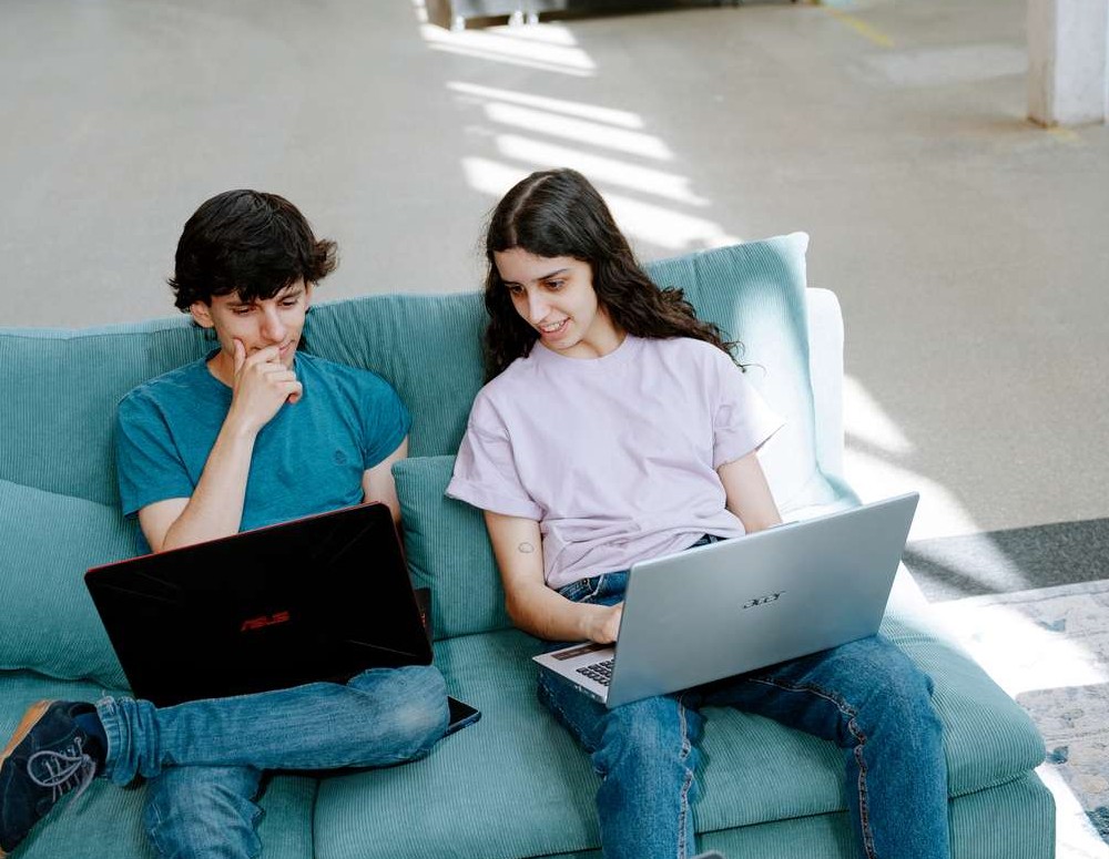 Two international students sitting in a sofa looking at the young man's laptop.