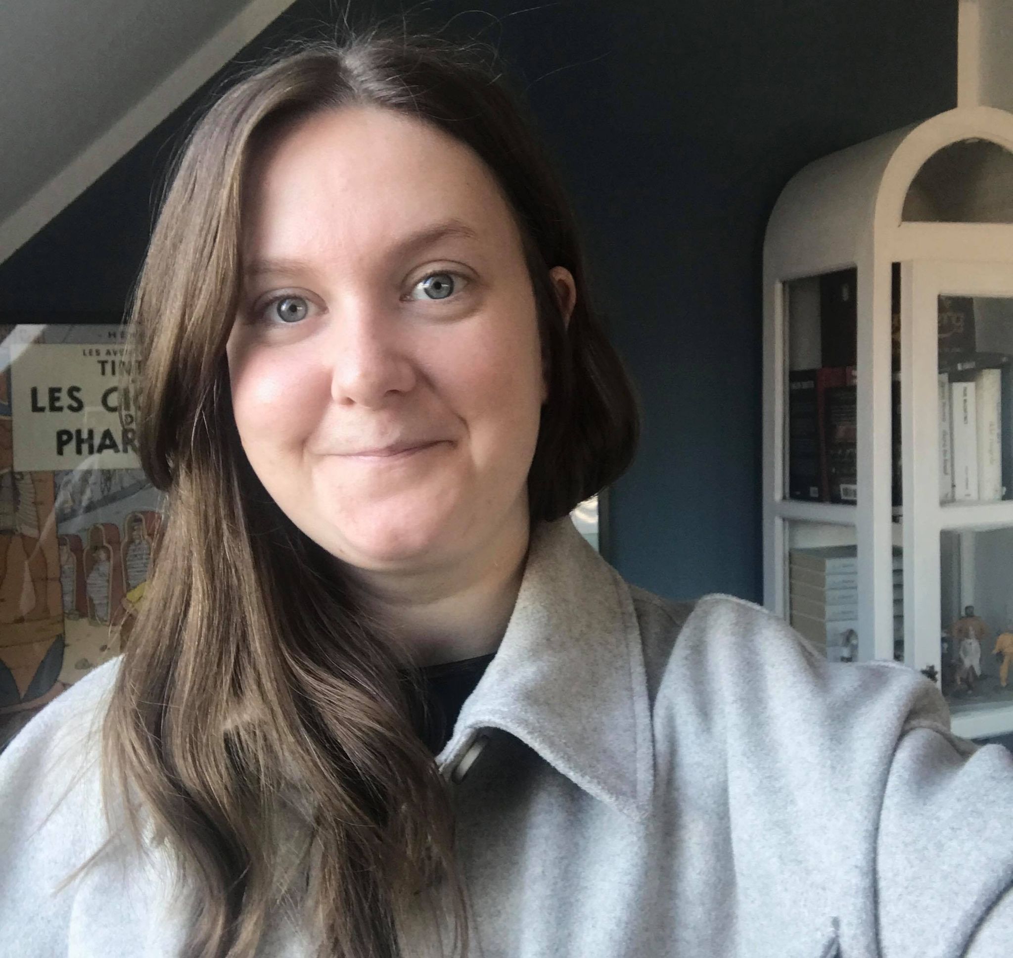katja kronvold fotograferet indendørs i en lys grå jakke foran en mørk væg og et hvidt vitrineskab.