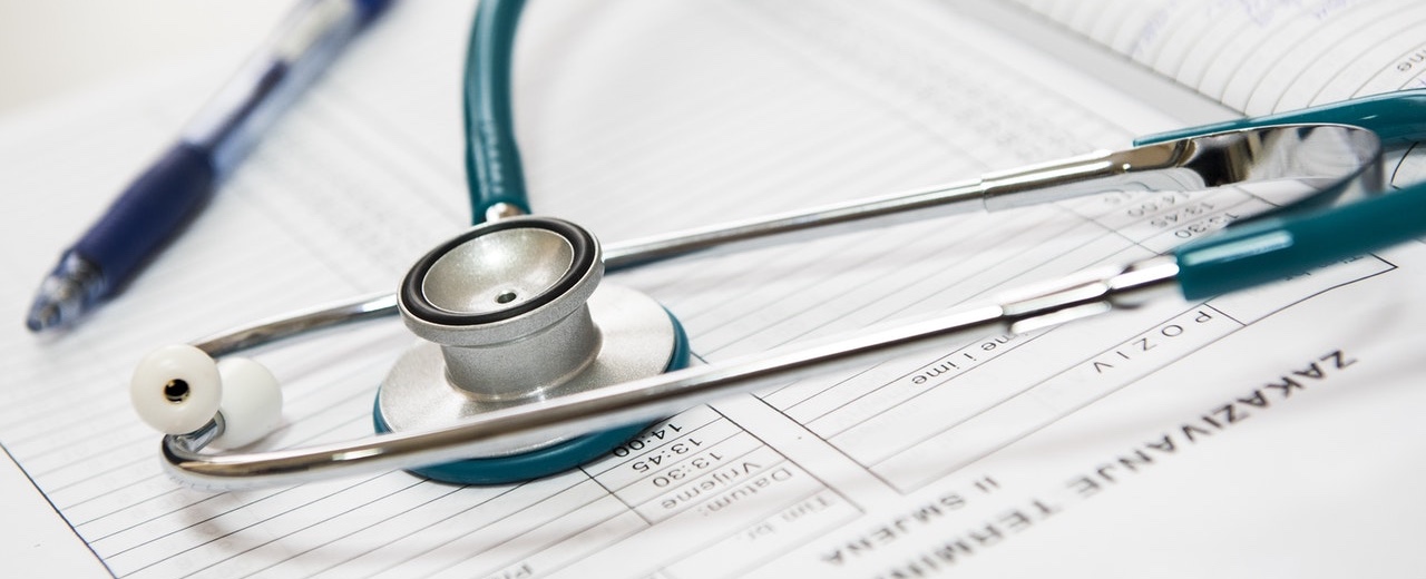 Stetoskop og blå kuglepen på medicinske dokumenter med synlig trykt tekst.