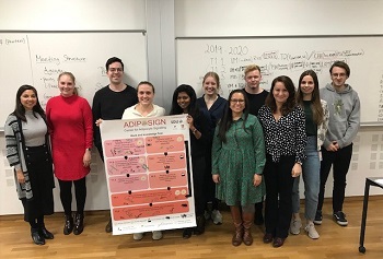 Group photo of people in a classroom holding a poster titled "ADIF SIGN" in front of whiteboards with handwritten notes.